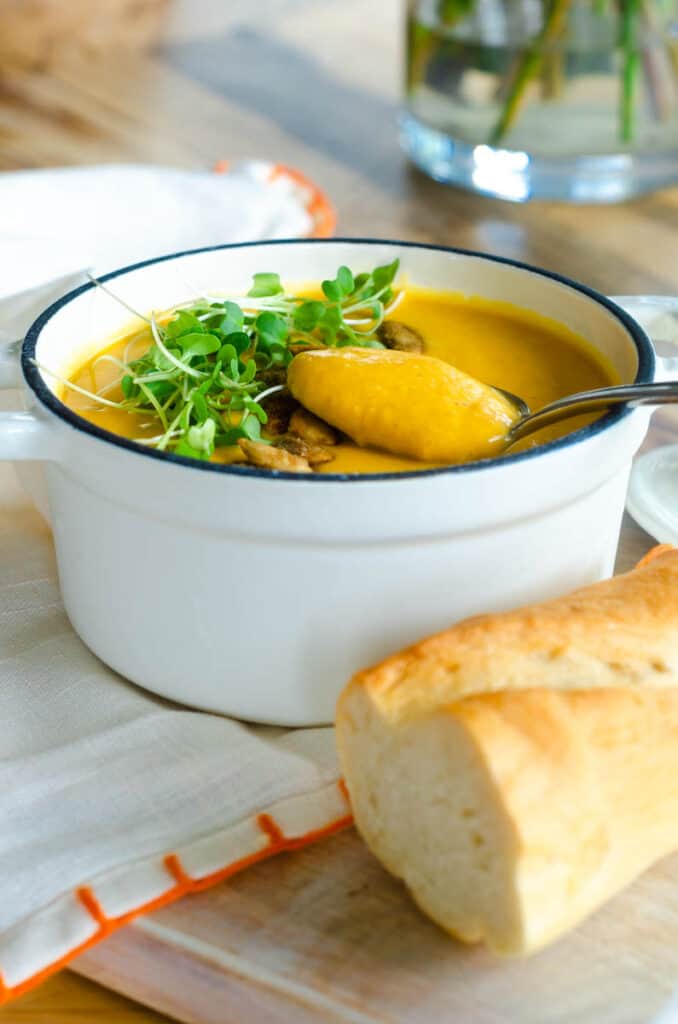 spoonful of pumpkin soup without cream over a white bowl and baguette. 