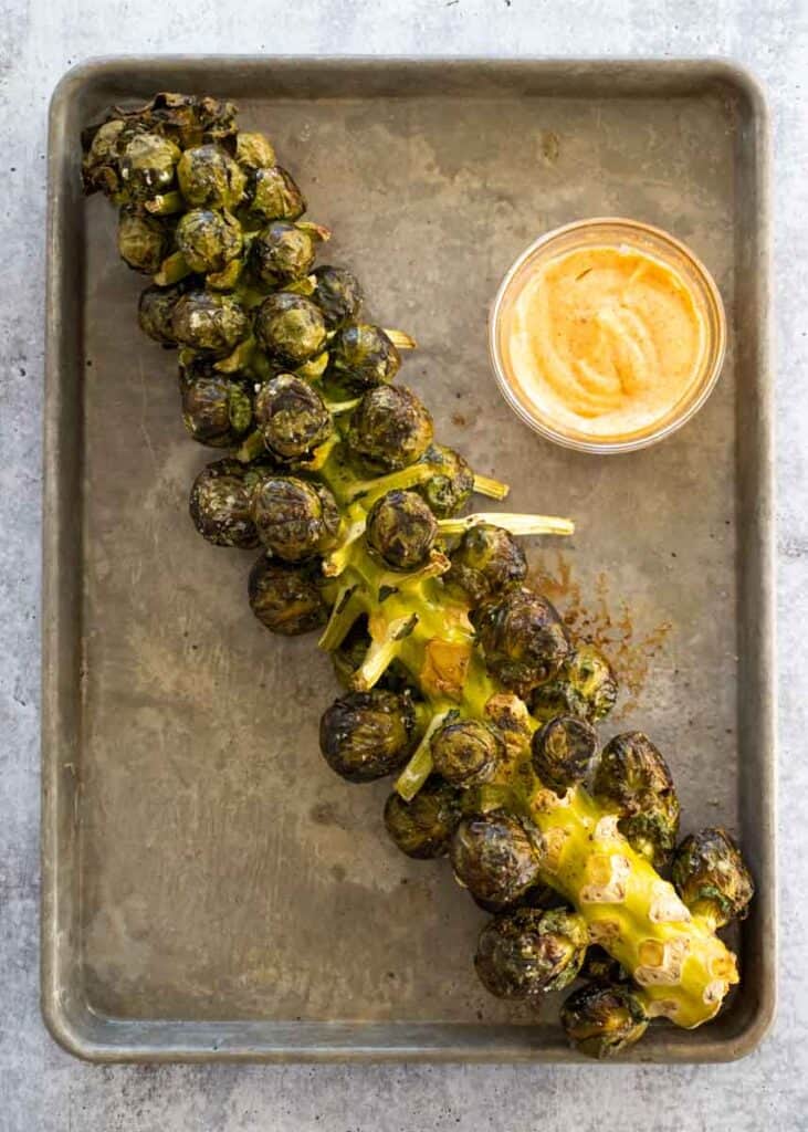 roasted brussels sprouts that just came out of the oven on a baking tray next to bowl of aioli. 