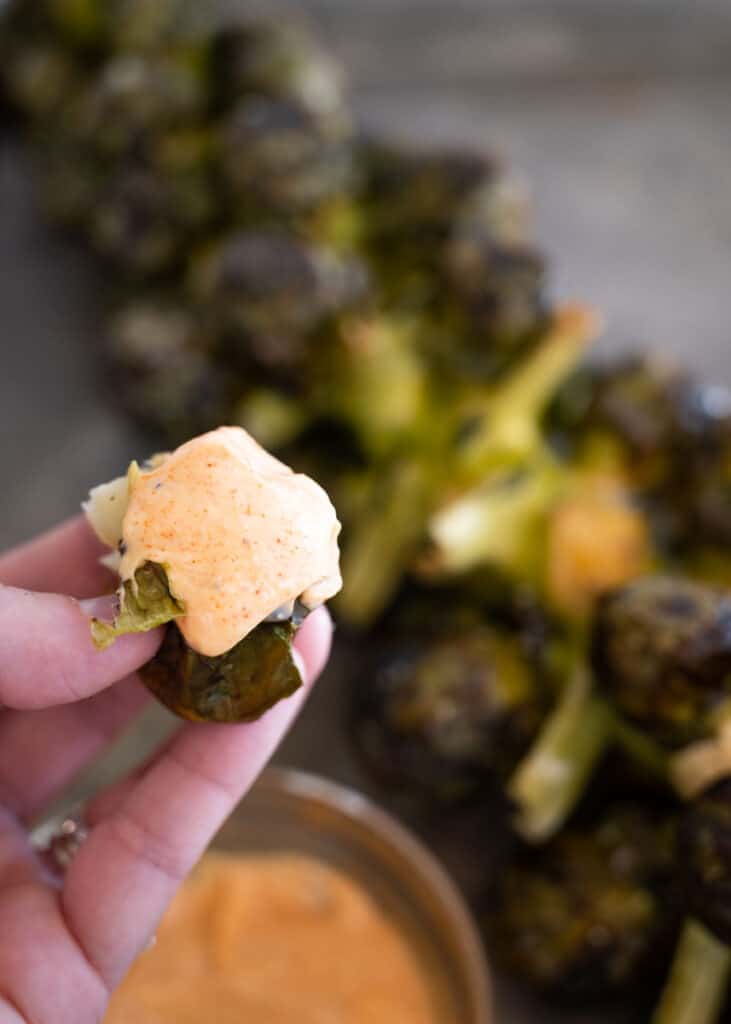 up close picture of dipped brussels sprout in an aioli in someone's hand. 