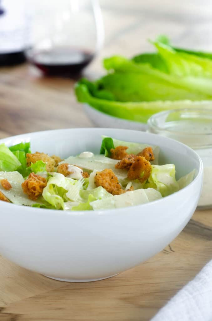 white bowl of caesar salad with croutons and parmesan cheese flakes.