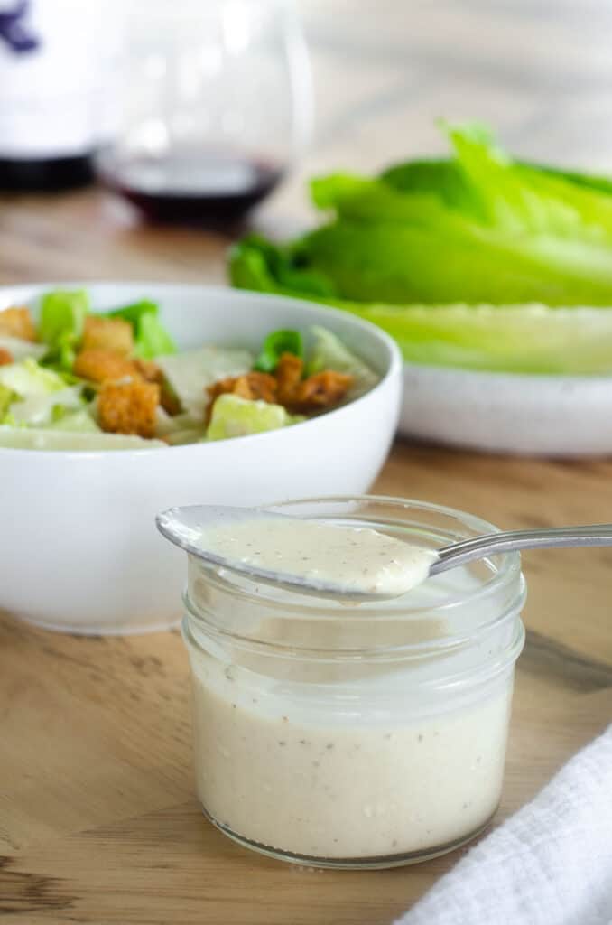 spoonful of caesar dressing resting on top of a glass jar of dressing. 