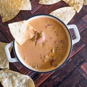 aerial picture of a small white dutch oven with chili cheese dip with a tortilla chip dipped in