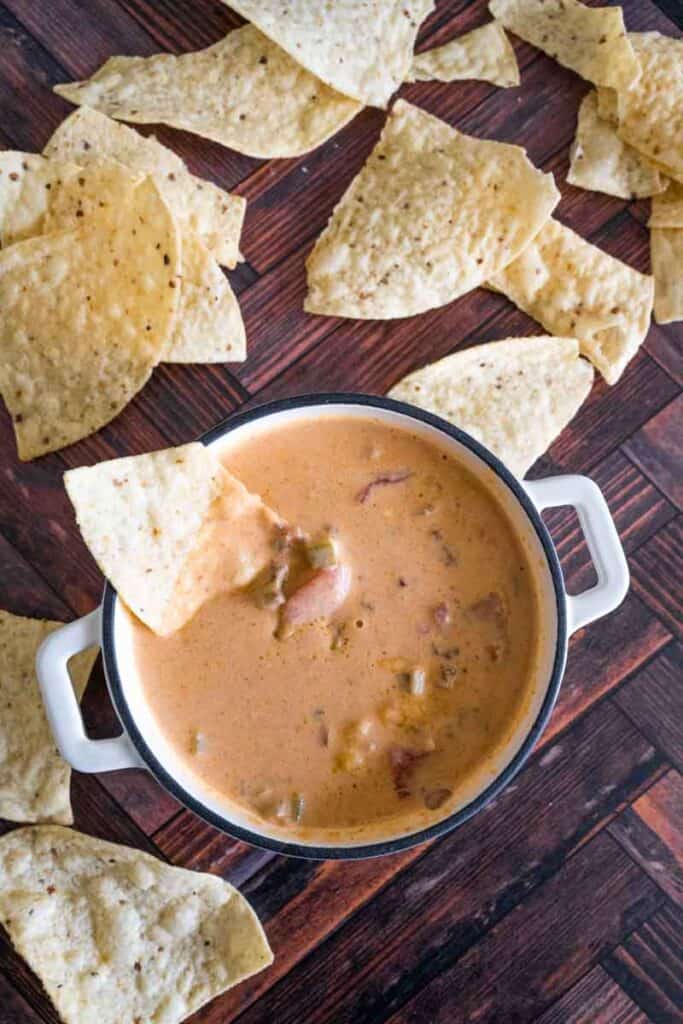 flat lay picture of a bowl of chili cheese dip with tortilla chips scattered around. 