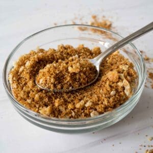 za'atar bread crumbs on a spoon over a clear bowl of breadcrumbs.