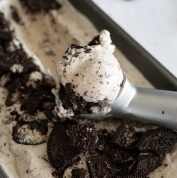 Up close scoop of Oreo cookie ice cream in front of container of the same ice cream.