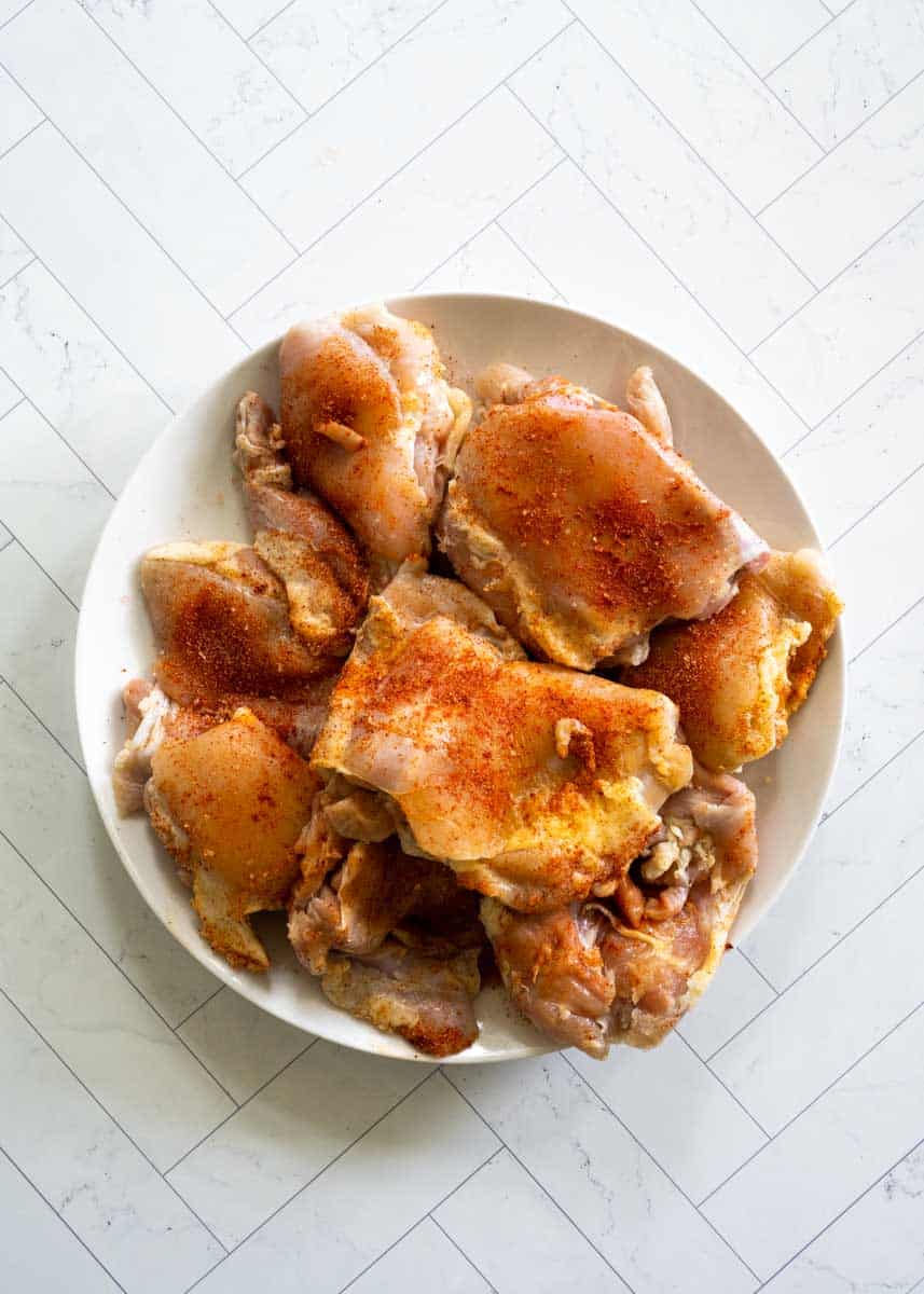 plate of raw chicken thighs that have been well seasoned on a white plate.