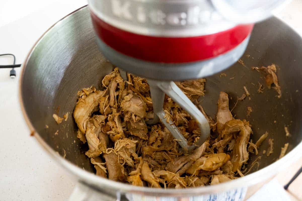 chicken thighs in a stand mixing bowl with a paddle attachment being shredded.