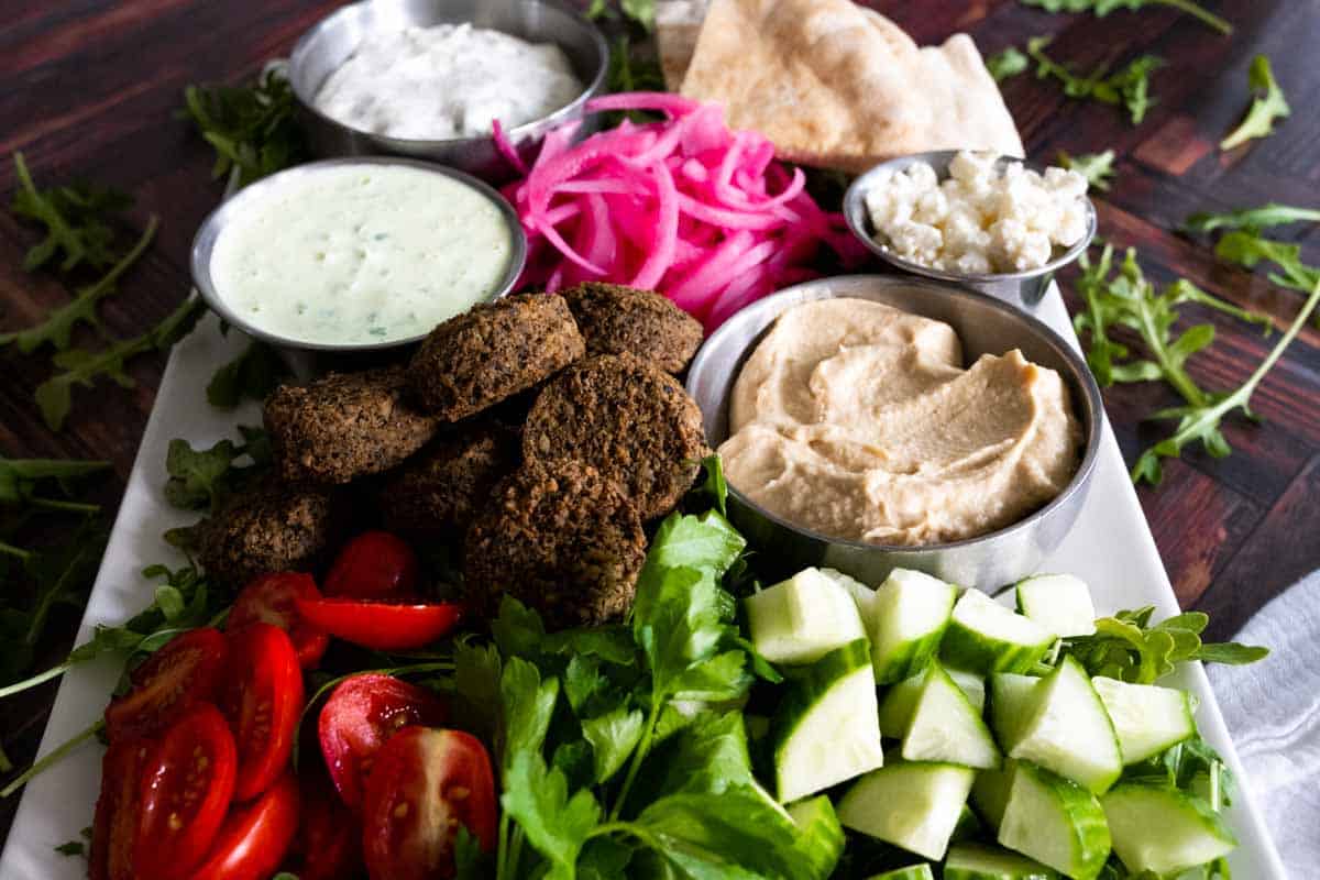 All of the ingredients for a falafel plate arranged neatly on white platter.
