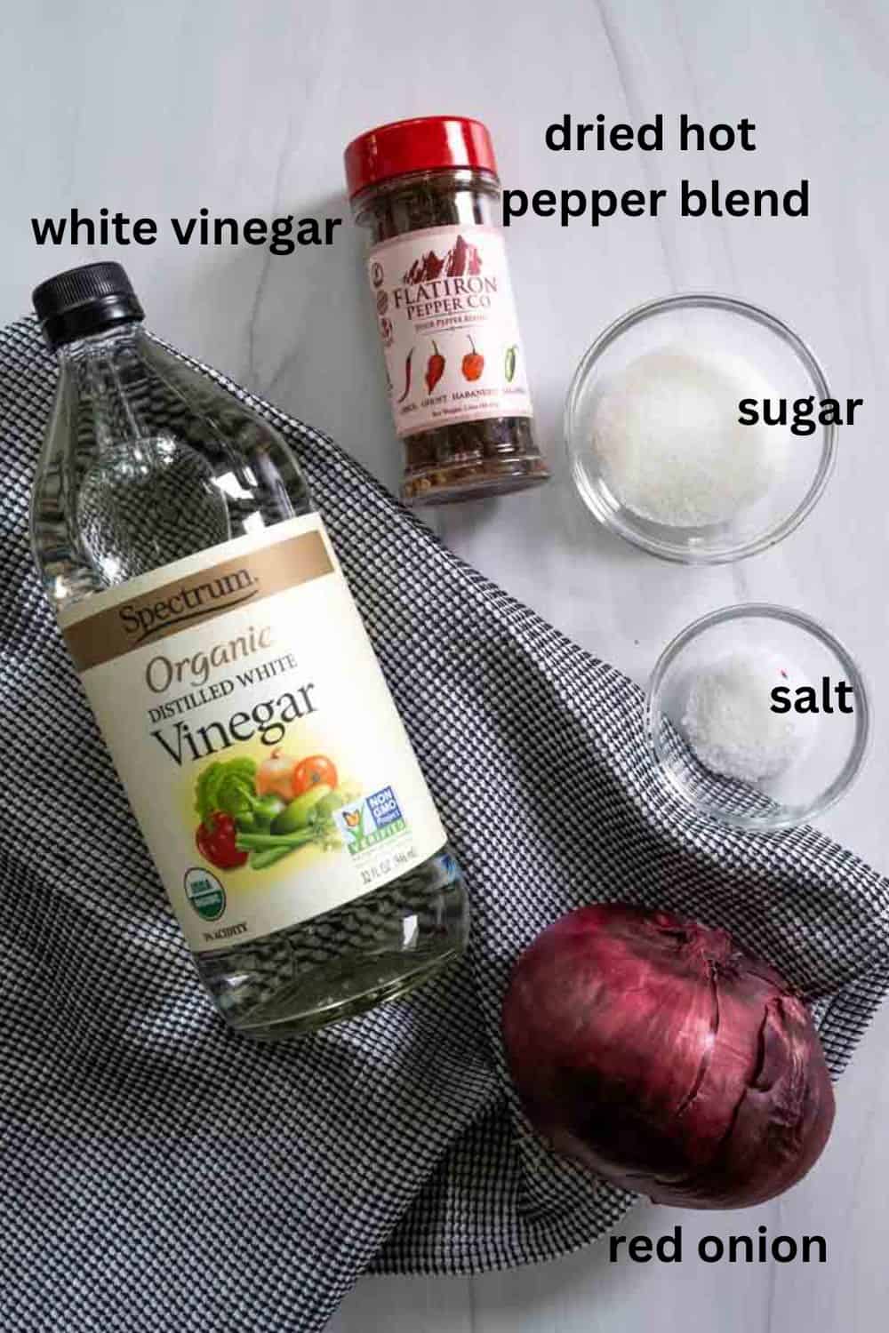 Ingredients needed for pickling onions, including vinegar, salt, sugar, hot peppers, and a red onion. 