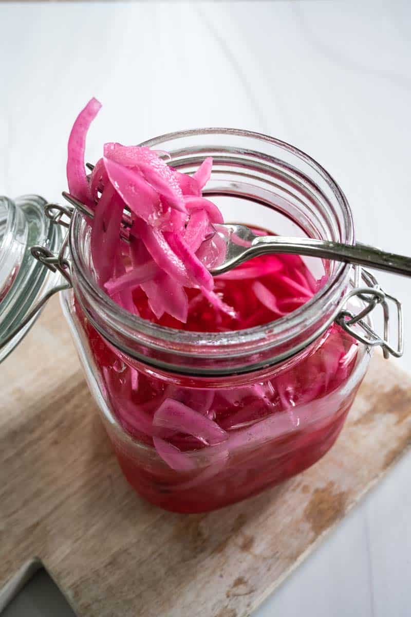 Jar of pickled red onions with a forkful of onions resting on top of the jar. 