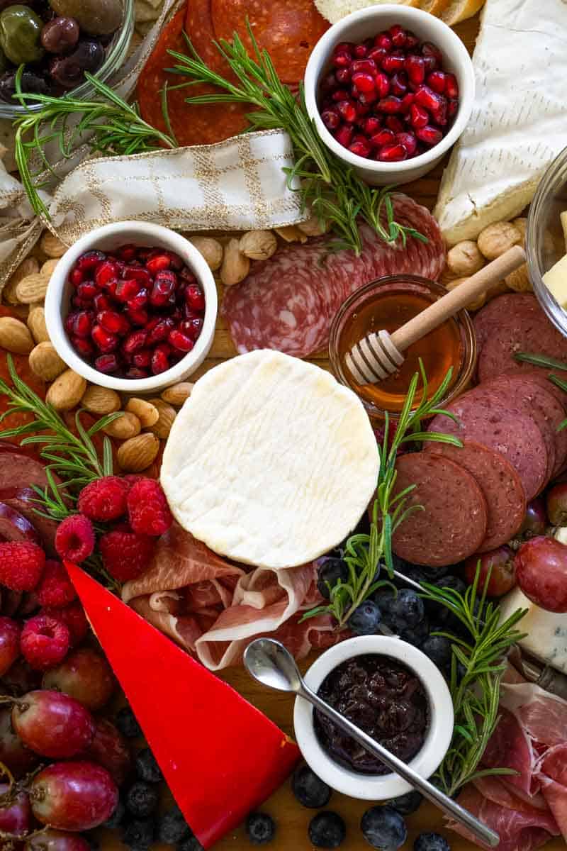 picture of charcuterie board with pomegranate, marcona almonds, brie, gouda, fresh raspberries, blueberries, salami, rosemary, and prosciutto. 