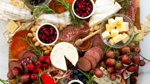 aerial view of large wooden charcuterie board covered with cheeses, meats, pomegranates, and other fruits and veggies.