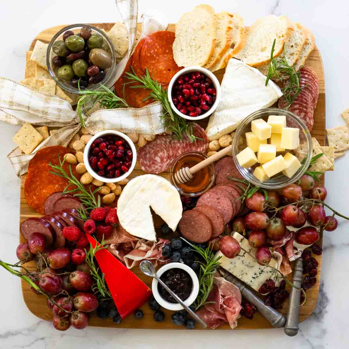 aerial view of large wooden charcuterie board covered with cheeses, meats, pomegranates, and other fruits and veggies.