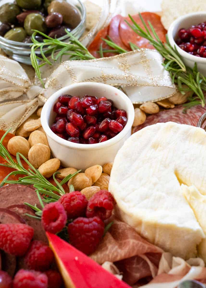 picture of a white container of fresh pomegranate seeds on a charcuterie board. 
