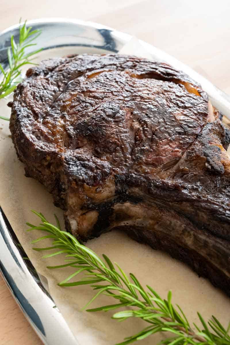 up close picture of fully grilled tomahawk steak next to sprig of rosemary. 