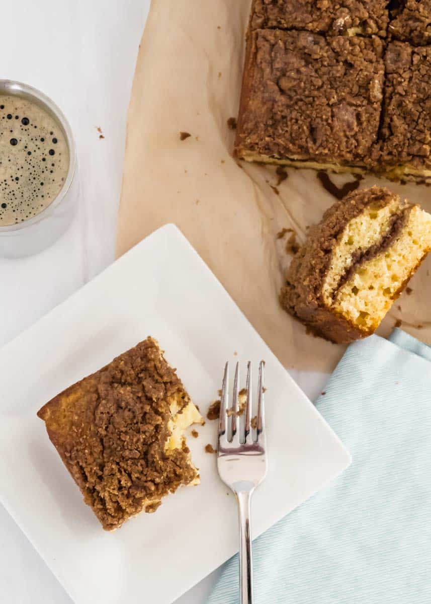 Slice of Greek yogurt coffee cake next to a messy fork and the rest of the coffee cake nearby. 