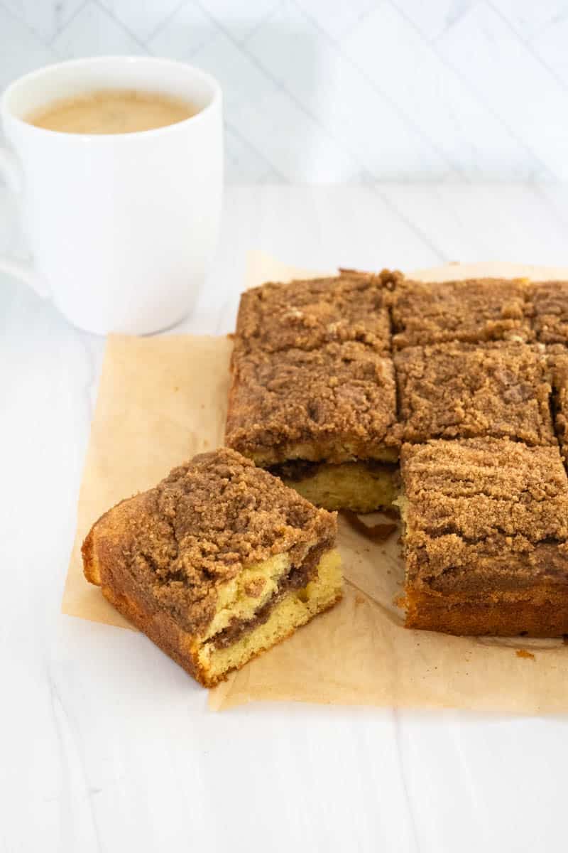 Square coffee cake that's been sliced into 9 equal pieces, with the bottom left corner angled to the side so you can see the crumb layer in the middle. 