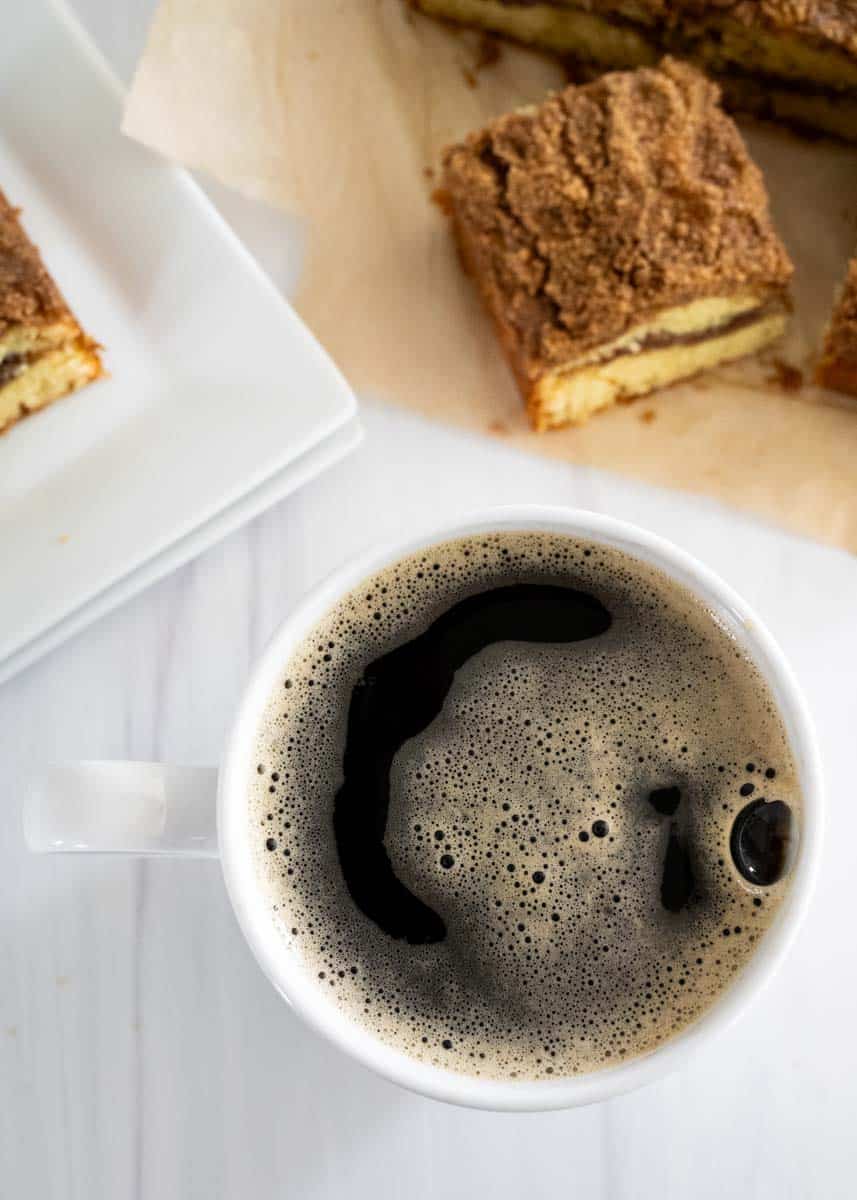 A cup of red eye coffee with a fresh baked coffee cake next to coffee mug. 