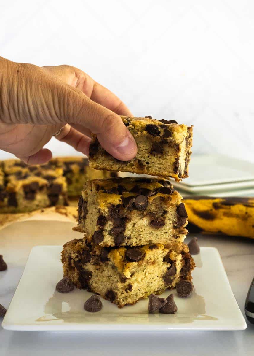 A hand picking up one piece of banana chocolate chip cake stacked on top of one another.