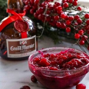 A bowl of cranberry relish with grand marnier with a bottle and winter berries in the background.