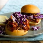 green plate with pulled pork with purple cabbage slaw on top and no top bun.