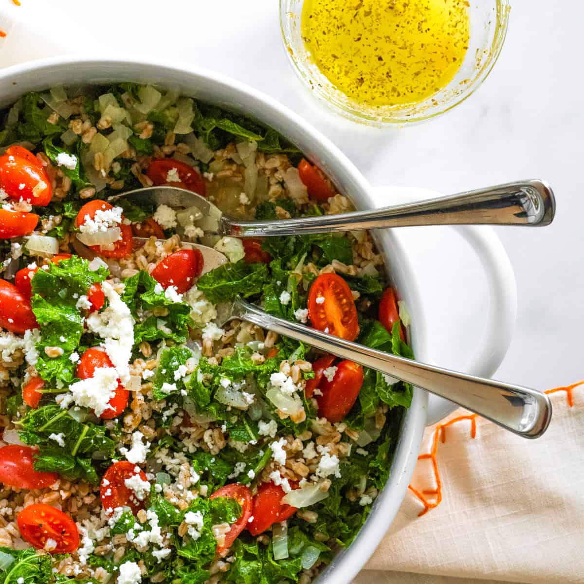 Large white serving bowl filled with kale and farro salad with grape tomatoes and goat cheese.
