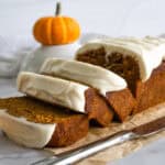 Up close picture of a sliced pumpkin loaf with cream cheese frosting and a small pumpkin in the background.