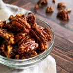 close up picture of a clear bowl full of candied pecans with a cream colored napkin underneath.