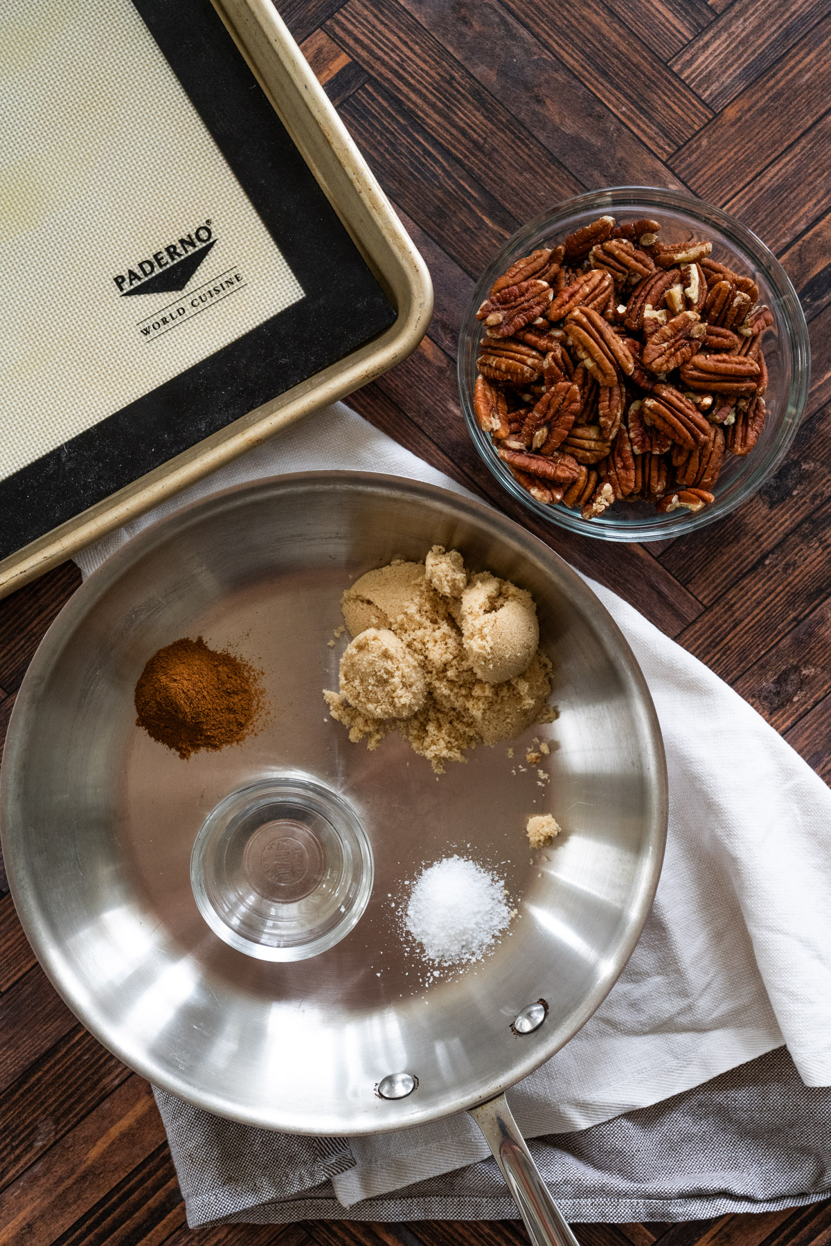 All of the ingredients you need to make candied pecans, including brown sugar, cinnamon, salt, vanilla extract, water, and pecans.