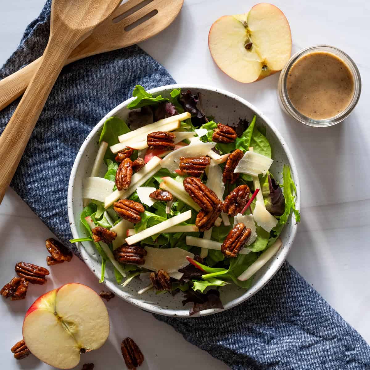 Flatlay of a large bowl of apple pecan salad with two halves of an apple around the plate, all underneath a blue cloth napkin