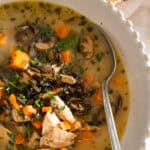 close up white bowl of turkey and wild rice soup with a spoon in the soup.