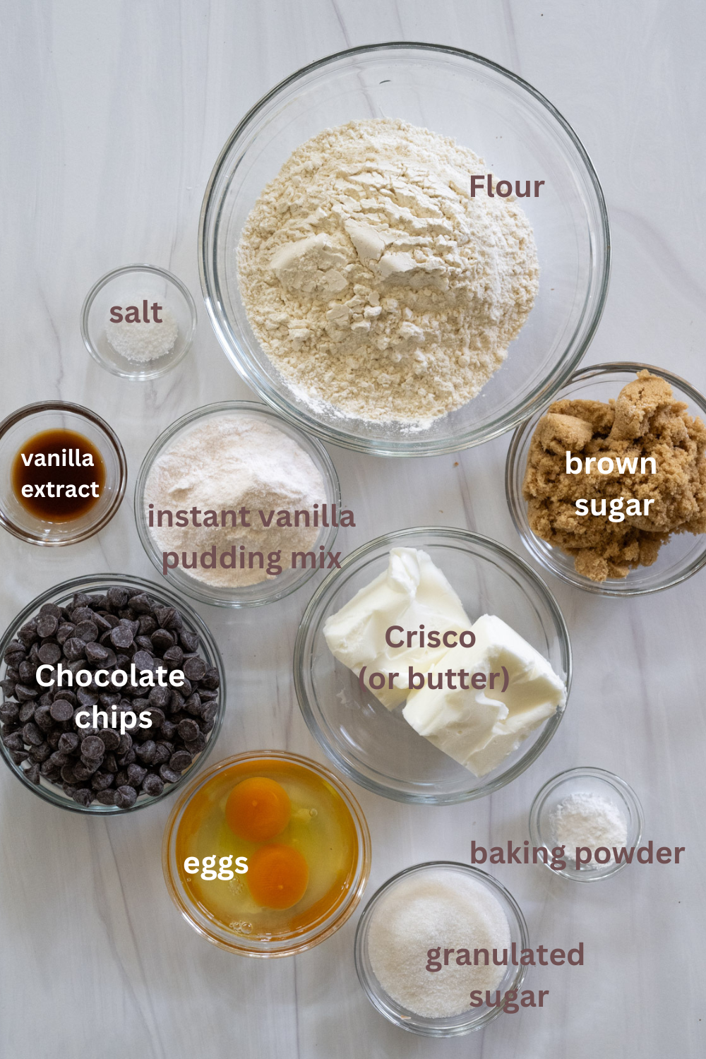 Lots of clear bowls with text overlay explaining all of the ingredients needed to make the cookies, including granulated sugar, baking powder, eggs, chocolate chips, Crisco or butter, brown sugar, instant vanilla pudding mix, vanilla extract, salt, and flour. 
