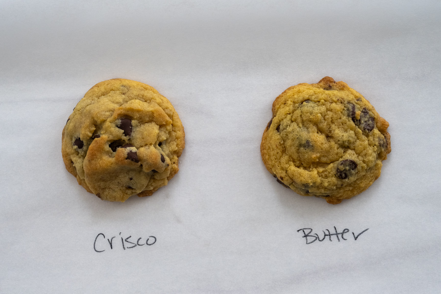 Two cookies ina  sheet of white parchment paper, with left labeled "Crisco" and the right labeled "butter." 