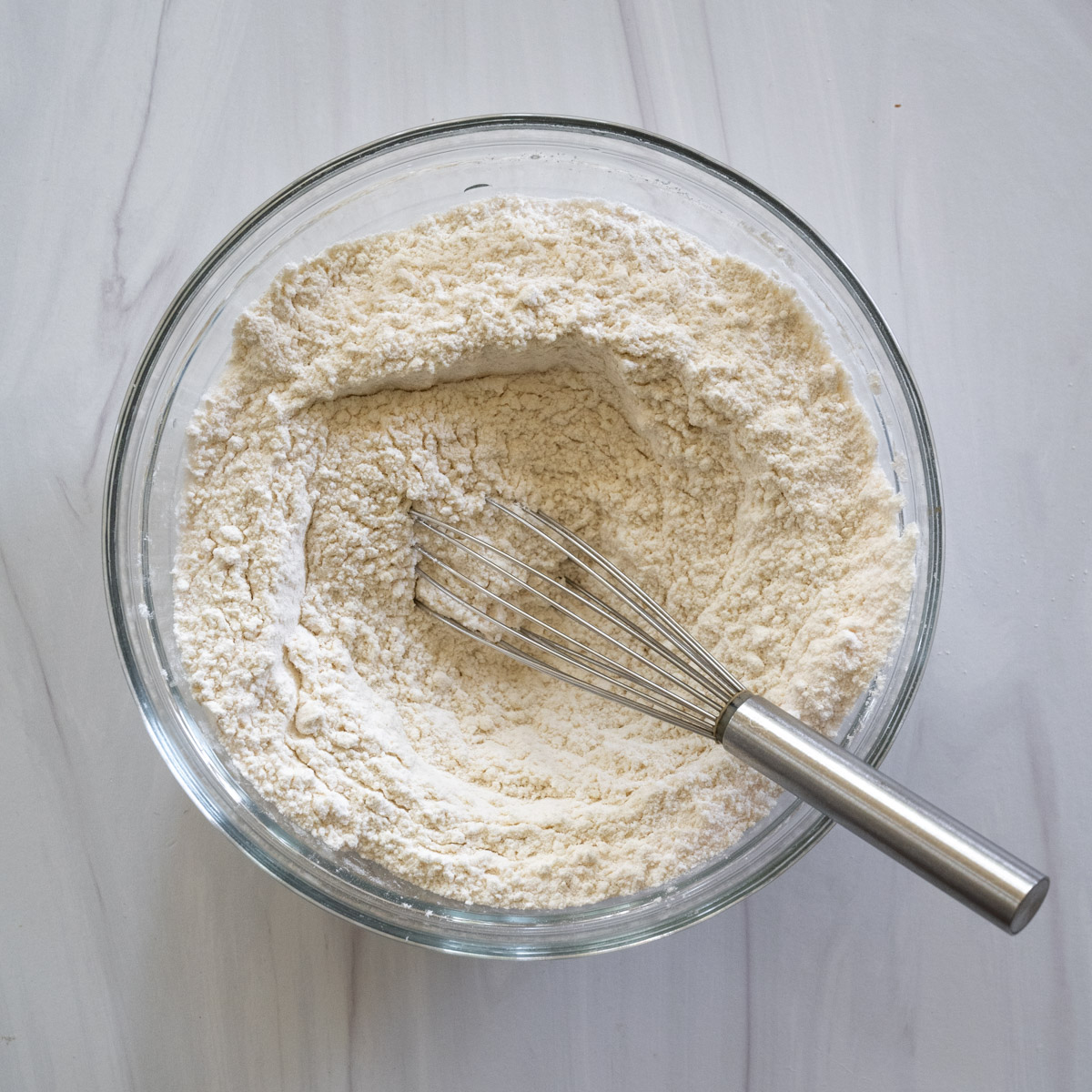 Step 1 showing the dry ingredients added to a clear bowl with a whisk in it. 