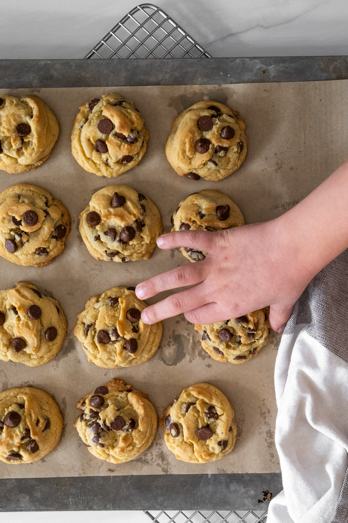 Baking tray of chocolate cookies lined with brown parchment paper and a child's hand grabbing one of the cookies. 