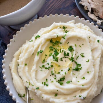 Large white bowl of mashed potatoes with a melted slab of butter and fresh parsley sprinkled on top.