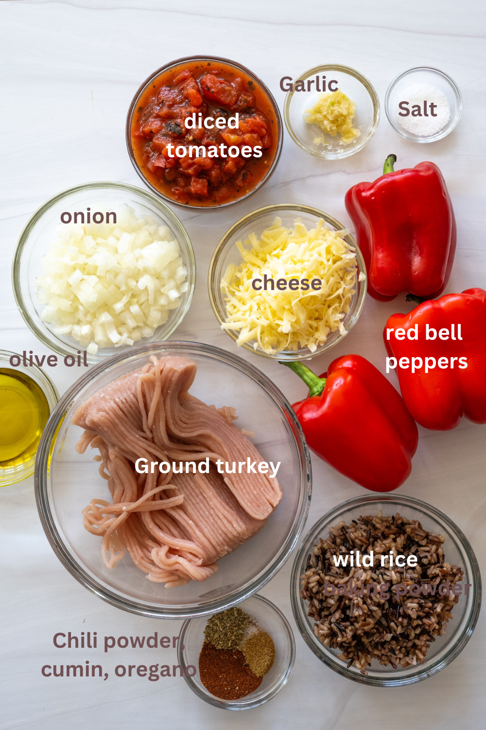 collage of ingredients needed to make ground turkey stuffed peppers, with text labeling ingredients, including wild rice, chili powder, cumin, oregano, ground turkey, olive oil, red bell peppers, cheese, onion, diced tomatoes, garlic, and salt. 