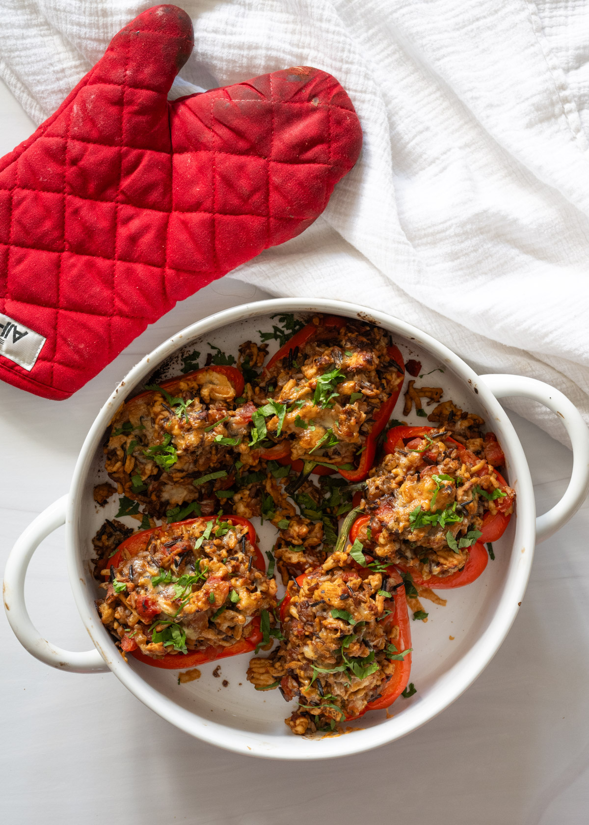 Ground turkey stuffed peppers after coming out of the oven and topped with fresh cilantro. an red oven mitt sits next to dish. 
