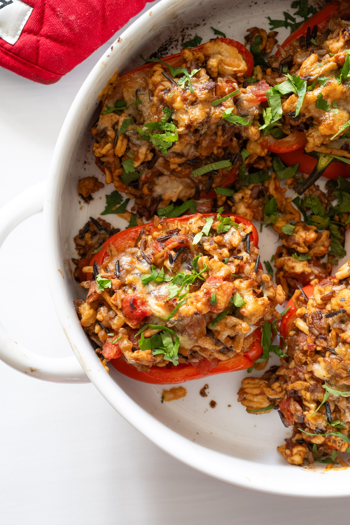 Large round bowl of stuffed peppers topped with chopped cilantro on a white background. 