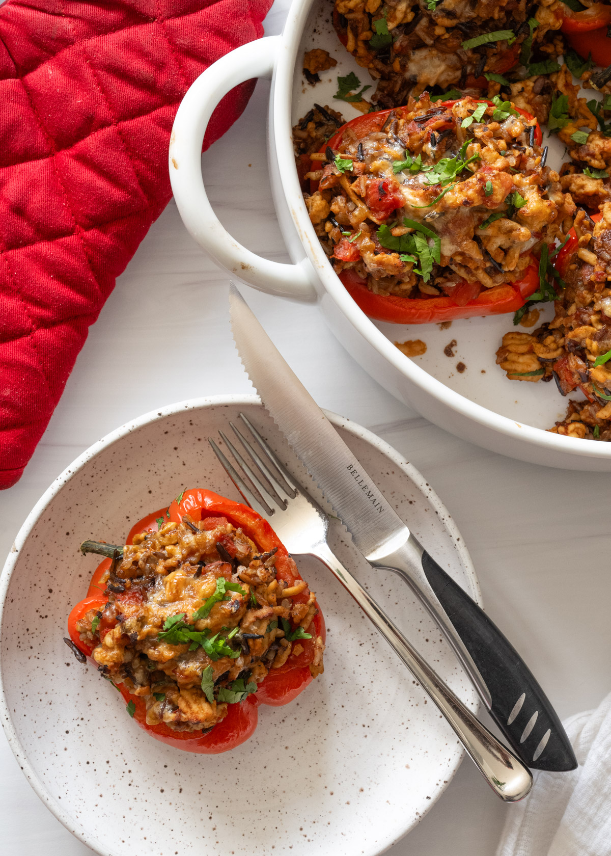 white speckled plate with one ground turkey stuffed pepper on it and a fork and knife next to it. 