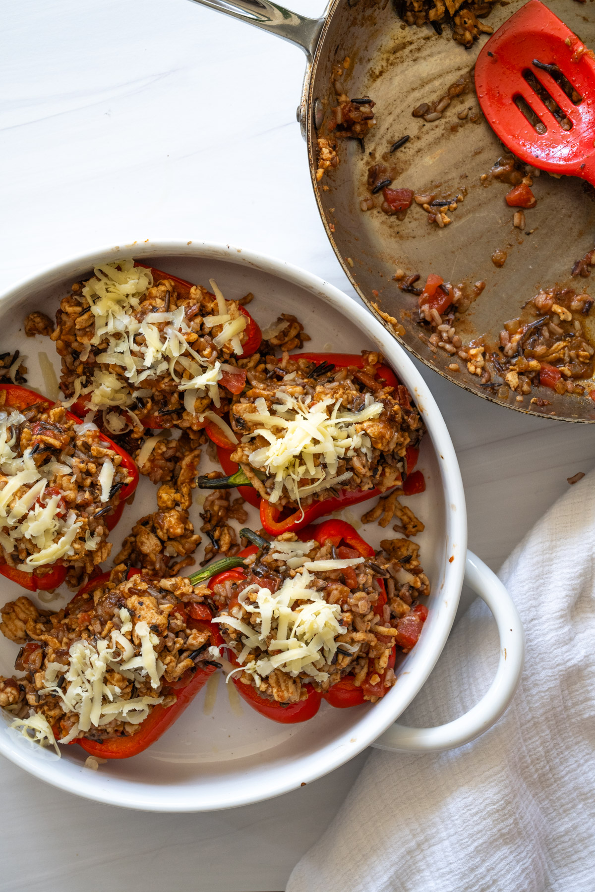 Step 7 of the directions showing red bell peppers stuffed with meat filling and topped with shredded cheese before baking. the pan with the filling is off to the side. 