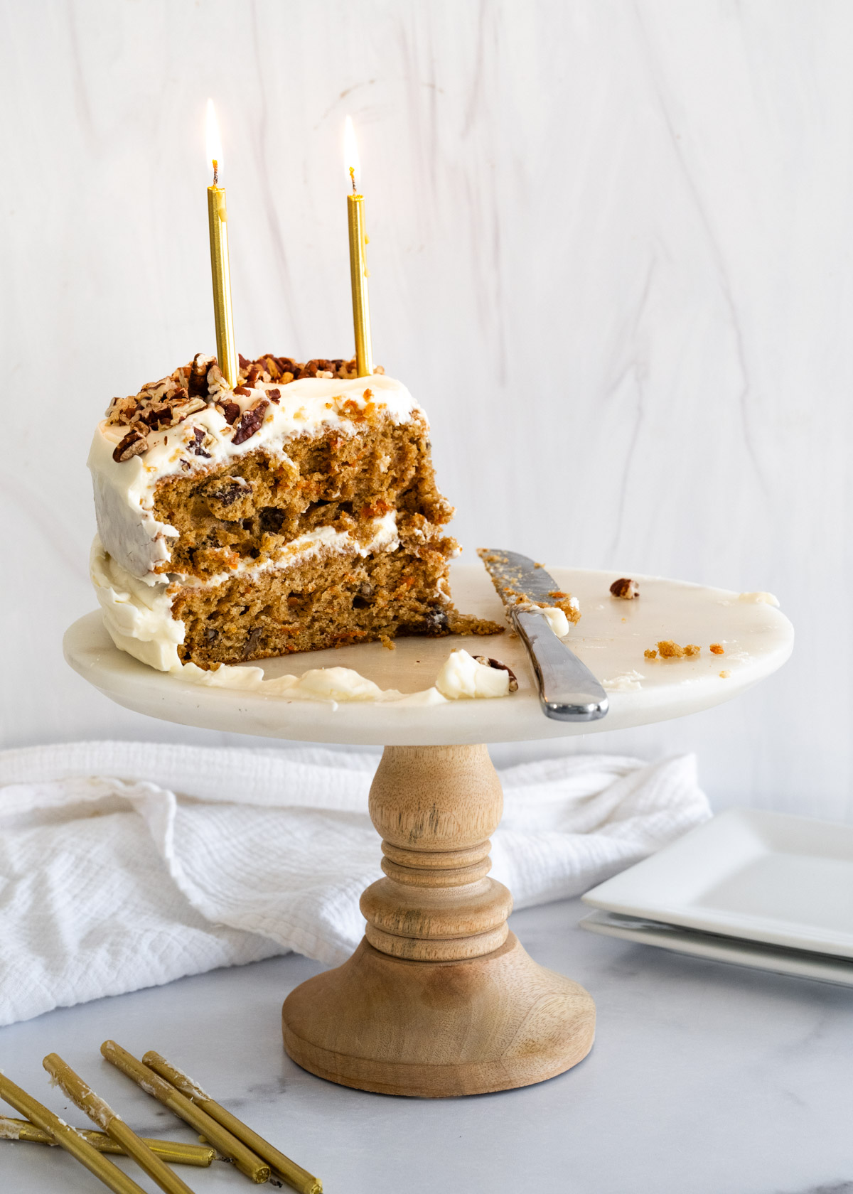 Cake platter holding a mostly eaten pecan carrot cake with a knife used for cutting next to the cake. 