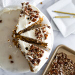 Aerial of three pieces of pecan carrot cake with a tray of toasted pecans and candles around the cake.