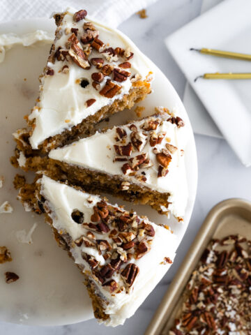 Aerial of three pieces of pecan carrot cake with a tray of toasted pecans and candles around the cake.