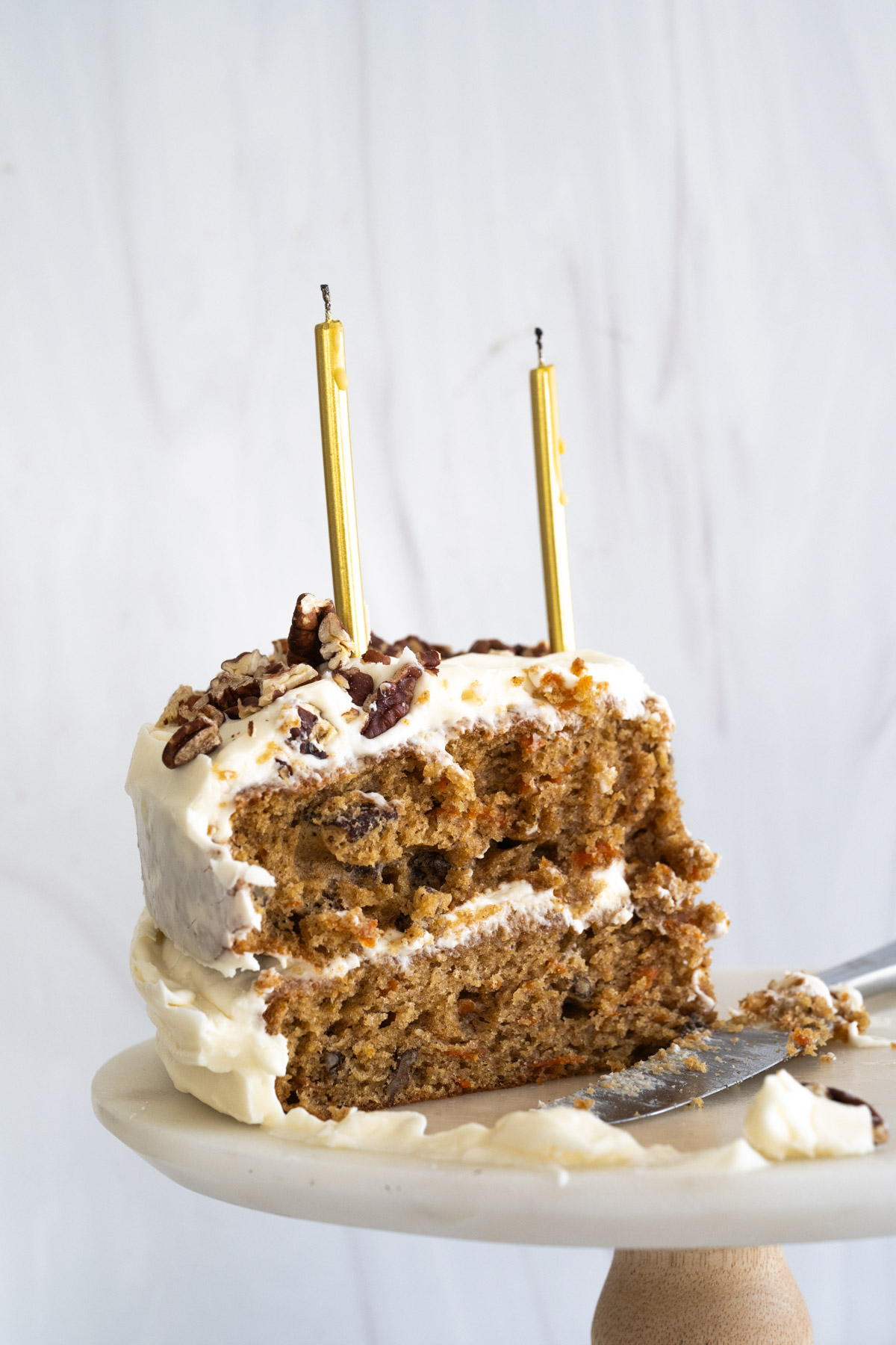 Up close picture of a slice of cake standing on a cake platter with two gold candles on top. 