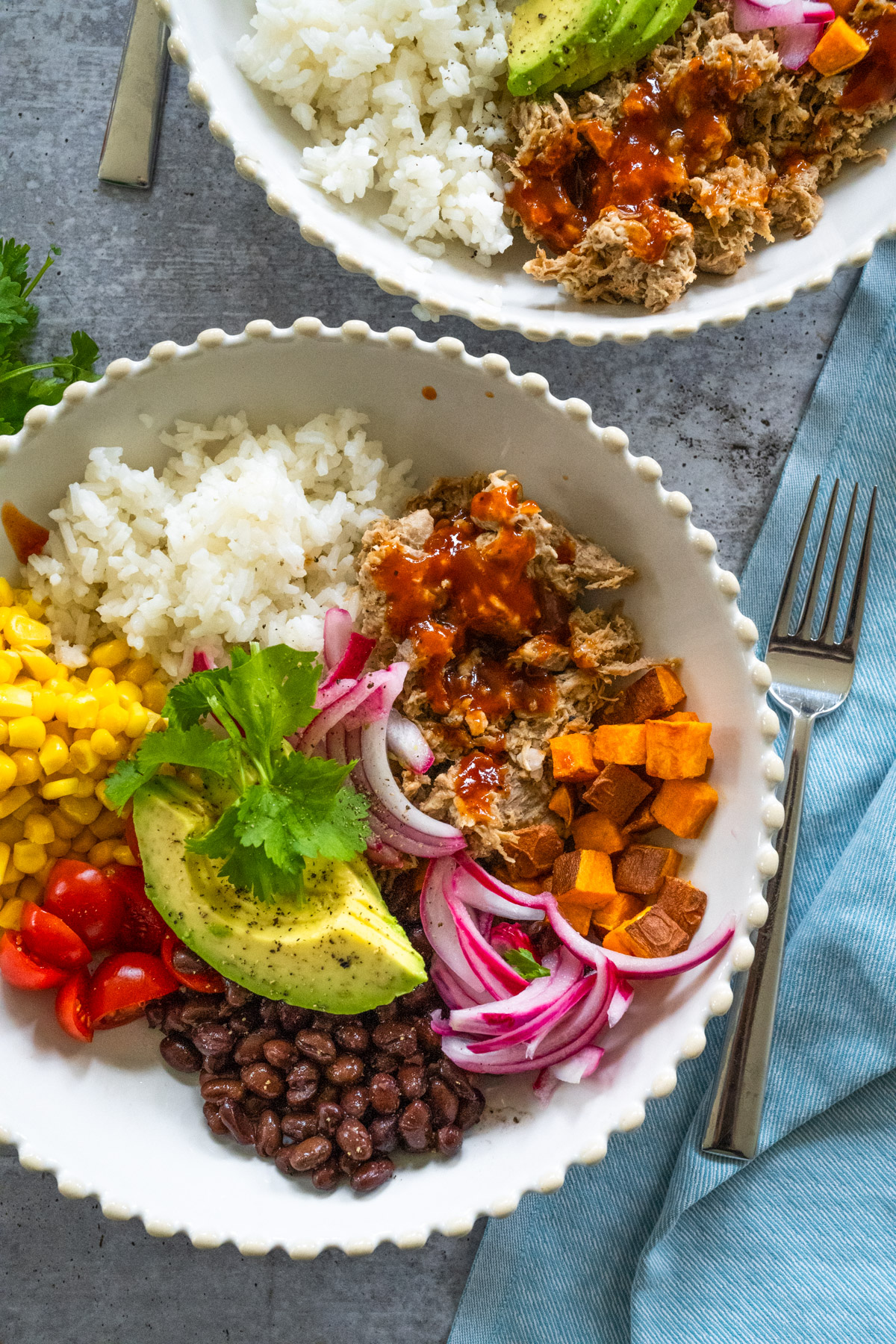 Close up picture of a white bowl with scalloped edges with BBQ pulled pork and all the fixings. 