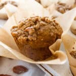 Up close picture of a pumpkin muffin with pecan streusel on top, unwrapped from the parchment muffin liner.