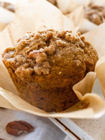 Up close picture of a pumpkin muffin with pecan streusel on top, unwrapped from the parchment muffin liner.