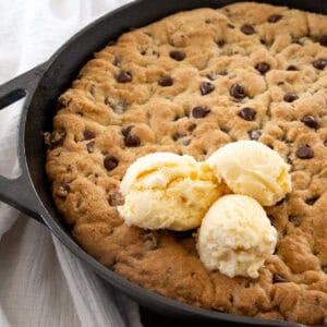 large chocolate chip skillet cookie fully cooked in a cast iron pan with three scoops of vanilla ice cream on top.