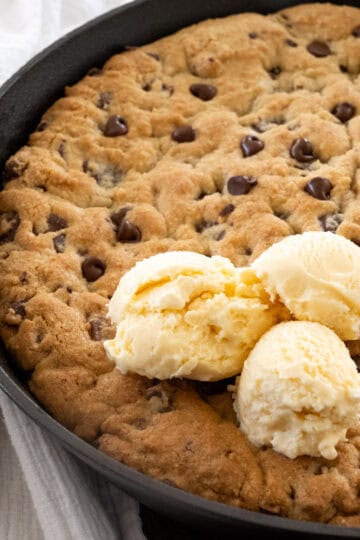 large chocolate chip skillet cookie fully cooked in a cast iron pan with three scoops of vanilla ice cream on top.